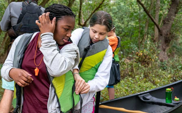 one student helps another adjust their PDF on a canoeing trip near DC